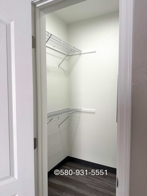 A white door is open to a small closet with two shelves.