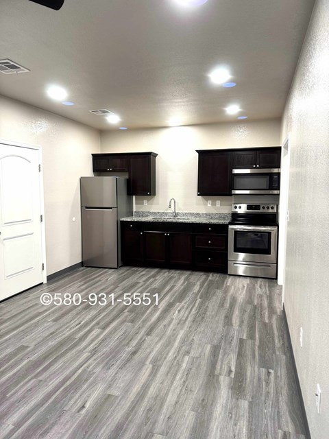 A kitchen with a refrigerator, microwave, oven, and sink.