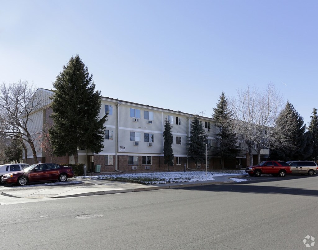 A red car is parked in front of a white building with a tree in front of it.