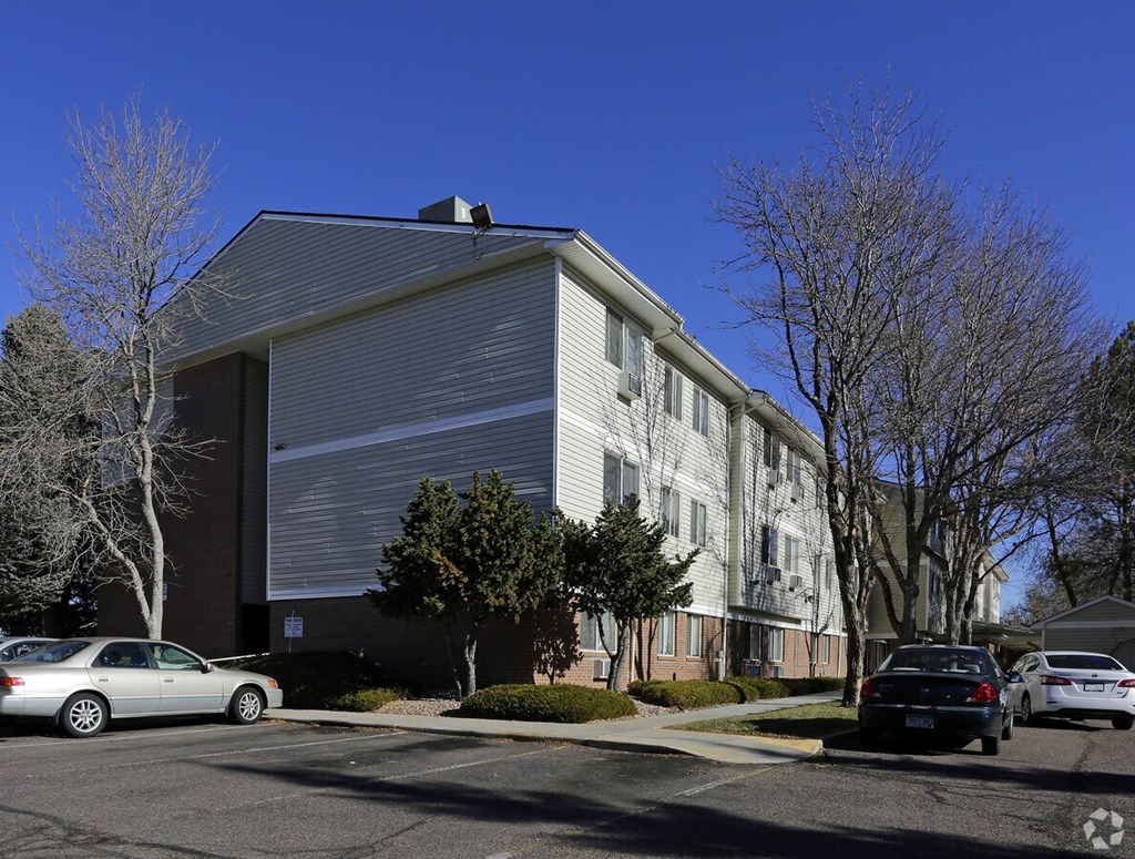 A silver car is parked in front of a grey building.