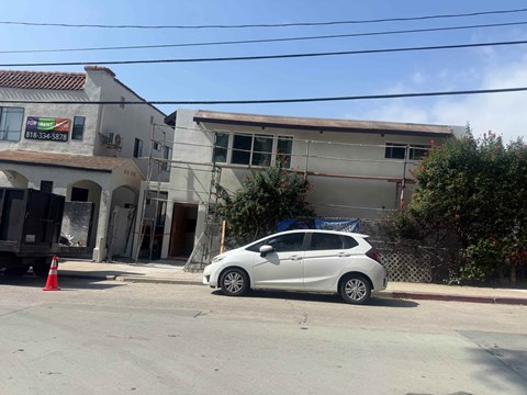 A white car is parked in front of a building with a phone number on it.
