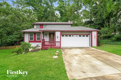A red and white house with a garage is surrounded by greenery.