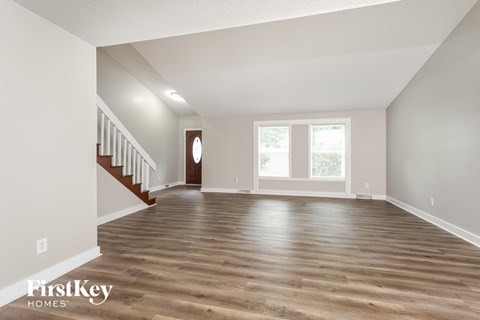 A spacious room with wooden floors and a staircase leading to another level.