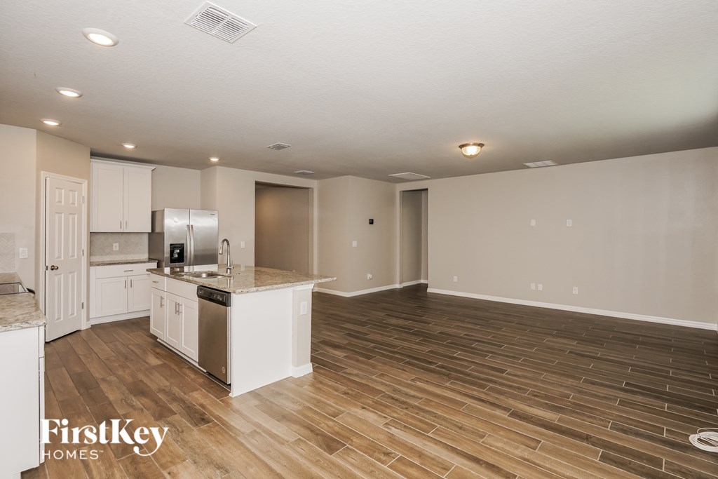 A spacious kitchen and living room with wooden flooring and white walls.