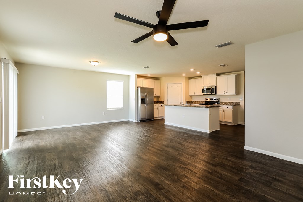 an empty living room with a ceiling fan and a kitchen