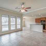an empty living room with a ceiling fan and a kitchen