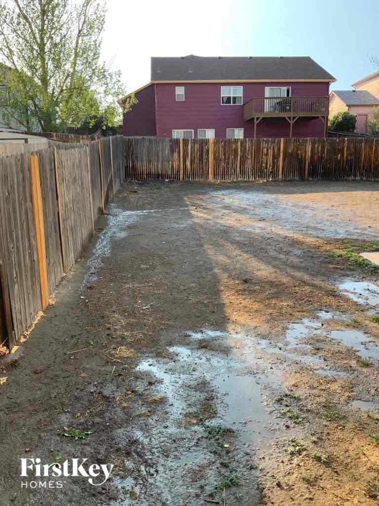 a yard with dirt and a fence with a house in the background