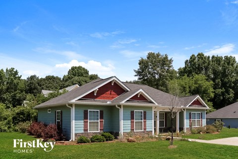a blue house with a red roof and green grass and trees