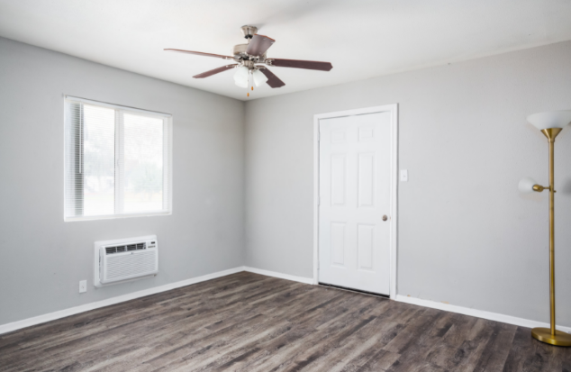 an empty living room with a ceiling fan and a white door