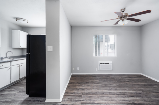 an empty living room with a ceiling fan and a kitchen