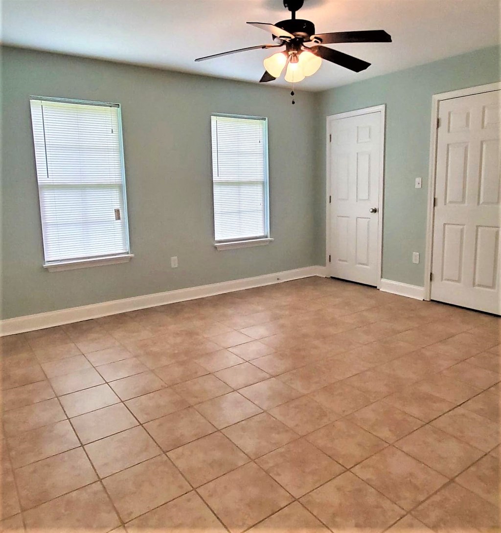 an empty living room with a ceiling fan and a tiled floor