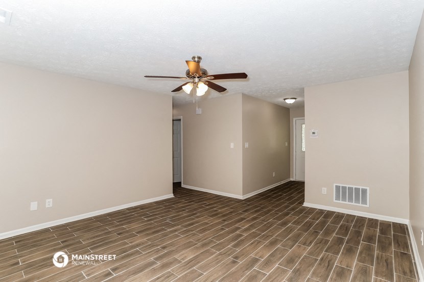 the spacious living room with wood flooring and a ceiling fan