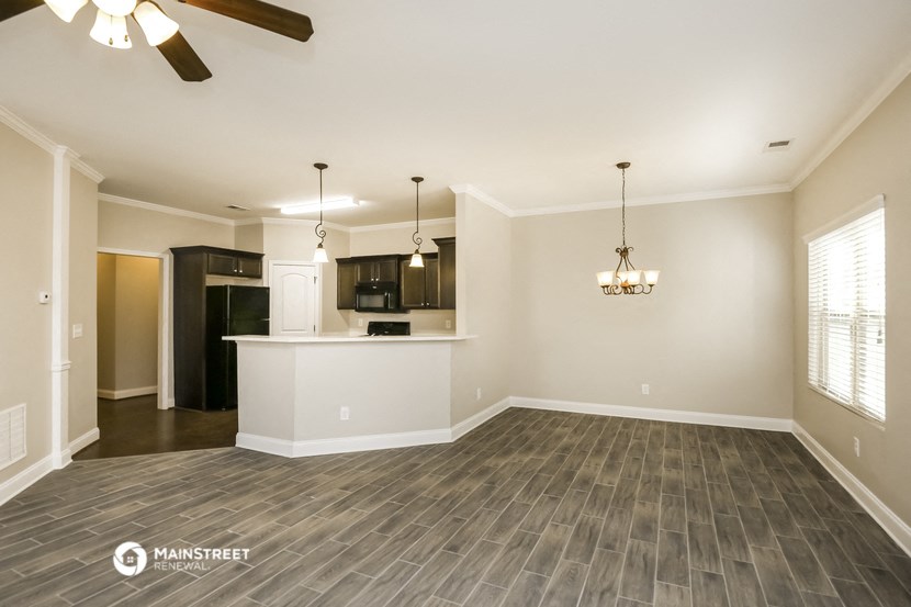 an empty living room with a kitchen and a ceiling fan