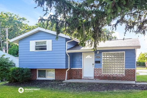 a blue and brick house with a white door and a tree