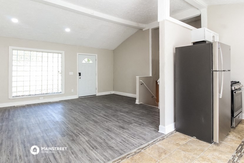 an empty living room with a refrigerator and a door