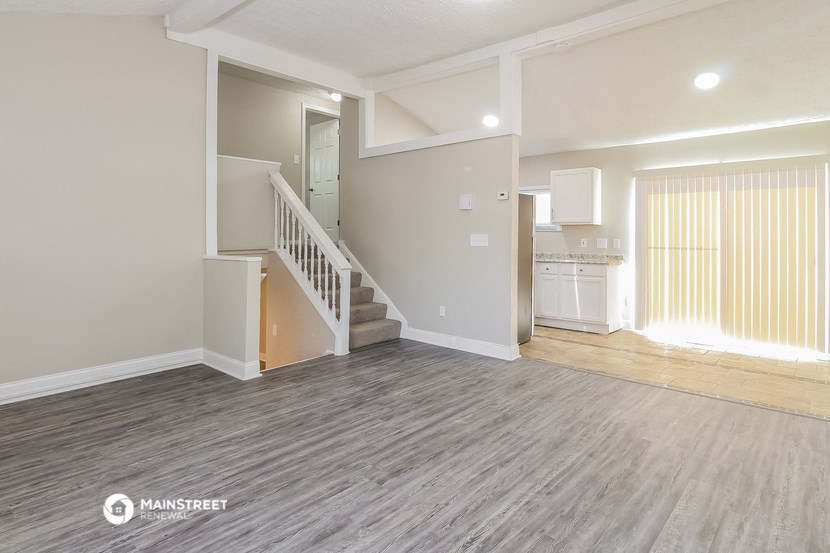an empty living room with a staircase and a kitchen