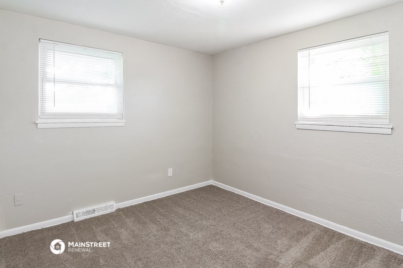 the bedroom of an apartment with carpet and two windows