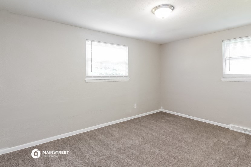 the spacious living room with two windows and carpeting