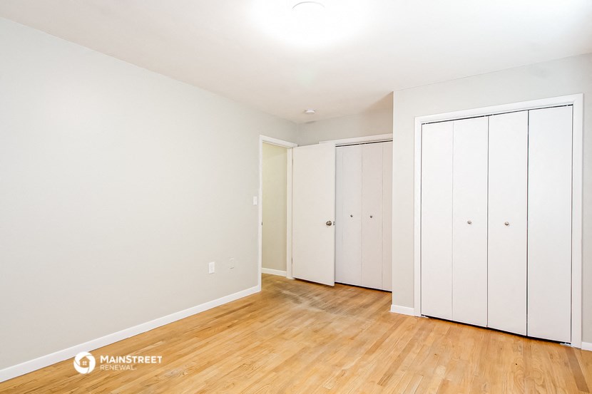 a bedroom with white walls and wood floors and white closets