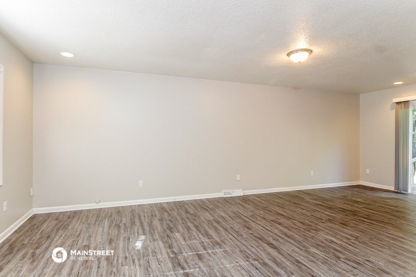 the spacious living room with wood flooring and white walls