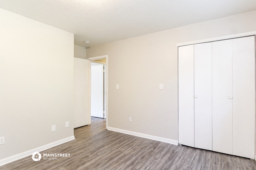 the living room of an apartment with white cabinets and wood flooring
