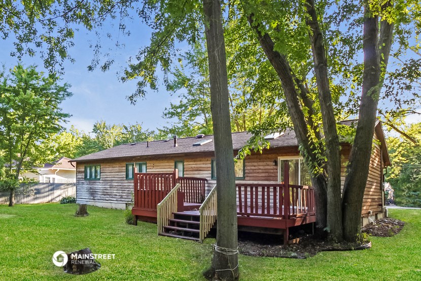 a wooden cabin with a deck in a yard with trees