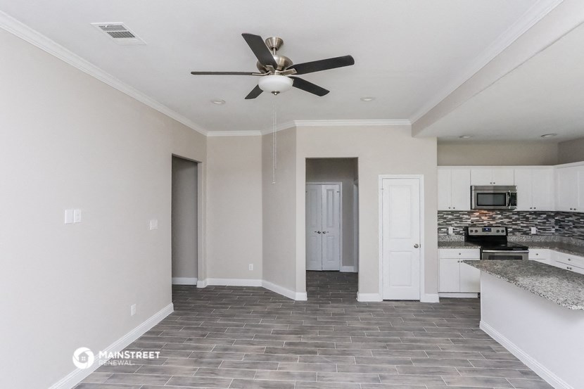 an empty living room with a ceiling fan and a kitchen