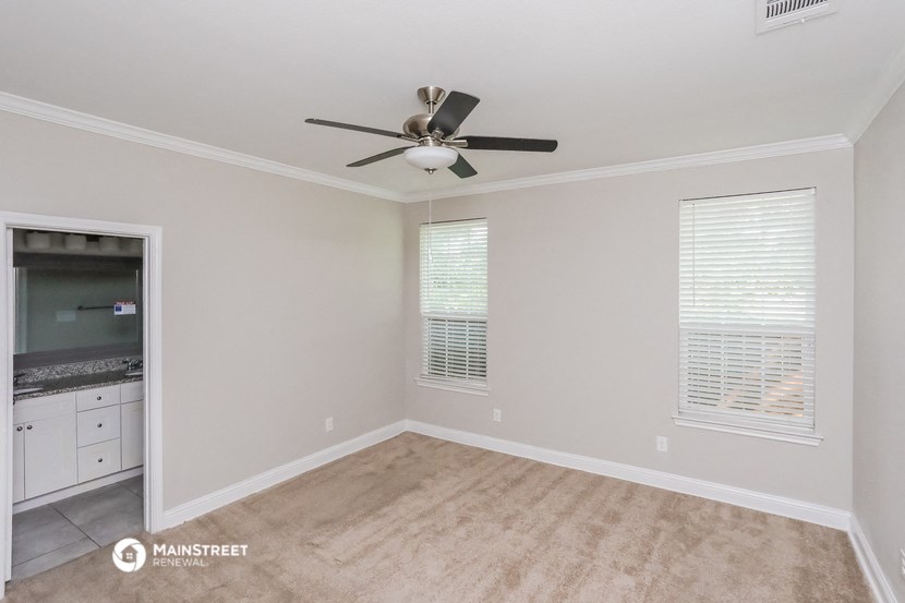 an empty living room with a ceiling fan and a kitchen