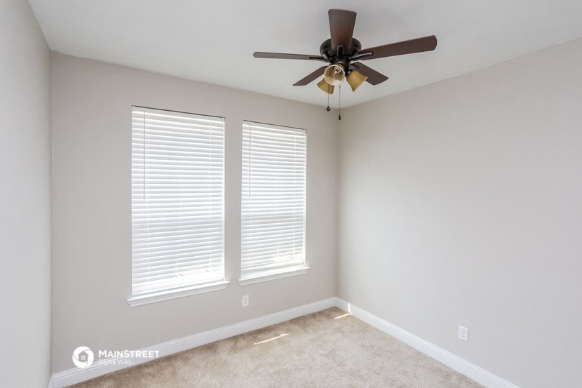 an empty room with a ceiling fan and two windows