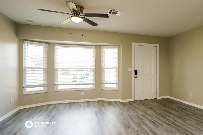 an empty living room with a ceiling fan and windows