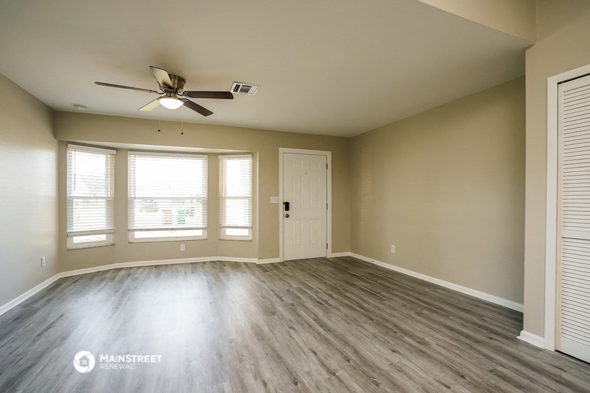 the spacious living room with wood flooring and a ceiling fan