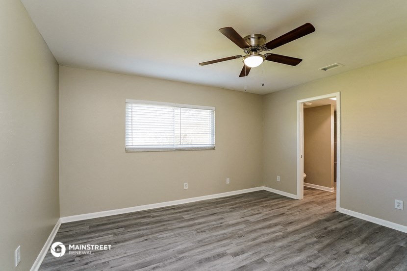 the spacious living room with wood flooring and a ceiling fan