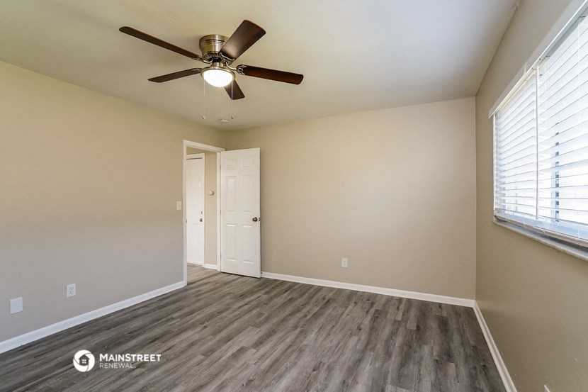 the spacious living room with wood flooring and a ceiling fan