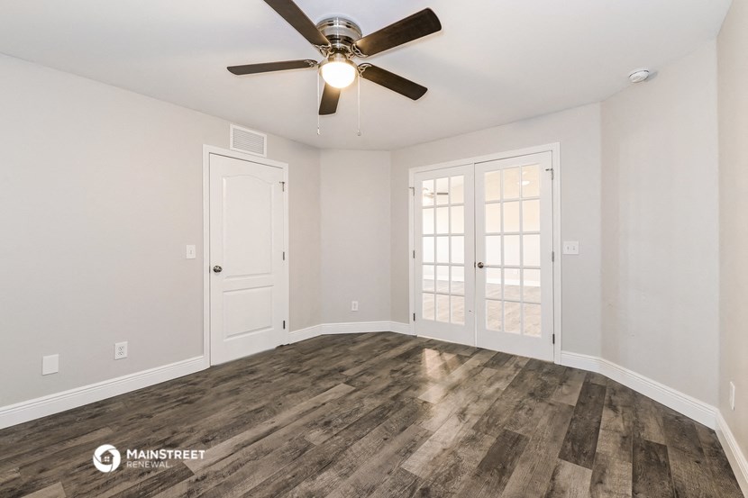 the spacious living room with wood flooring and a ceiling fan