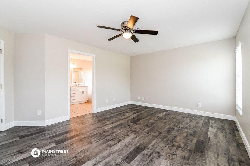 the spacious living room with wood flooring and a ceiling fan