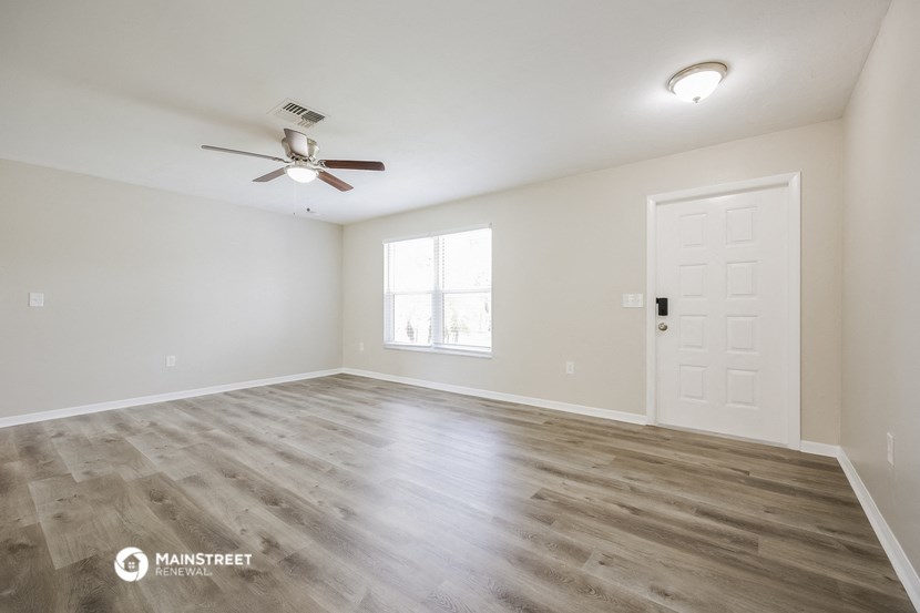 the spacious living room with wood flooring and a ceiling fan