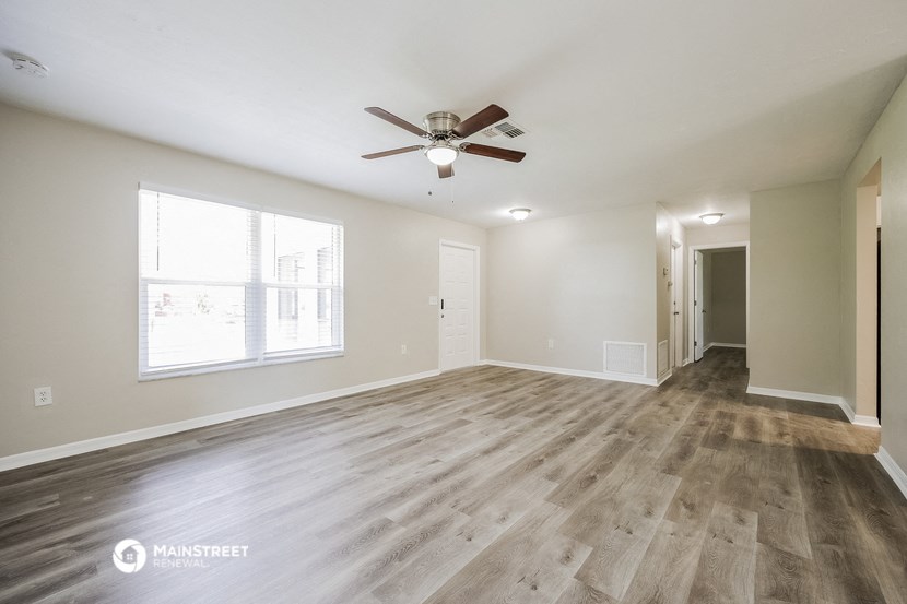 the spacious living room with wood flooring and a ceiling fan