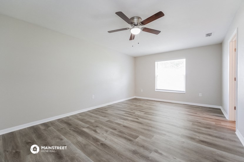 the spacious living room with wood flooring and a ceiling fan