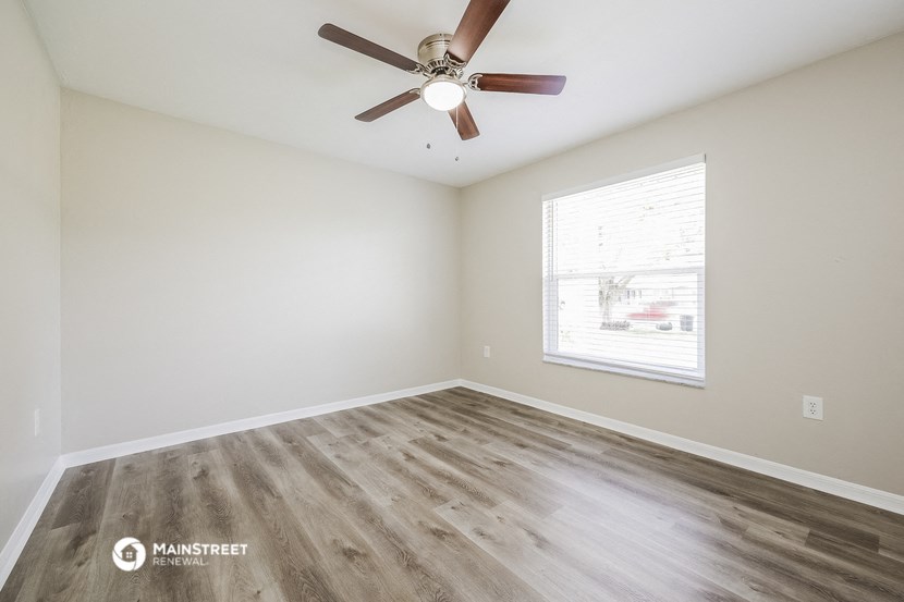 the spacious living room with wood flooring and a ceiling fan