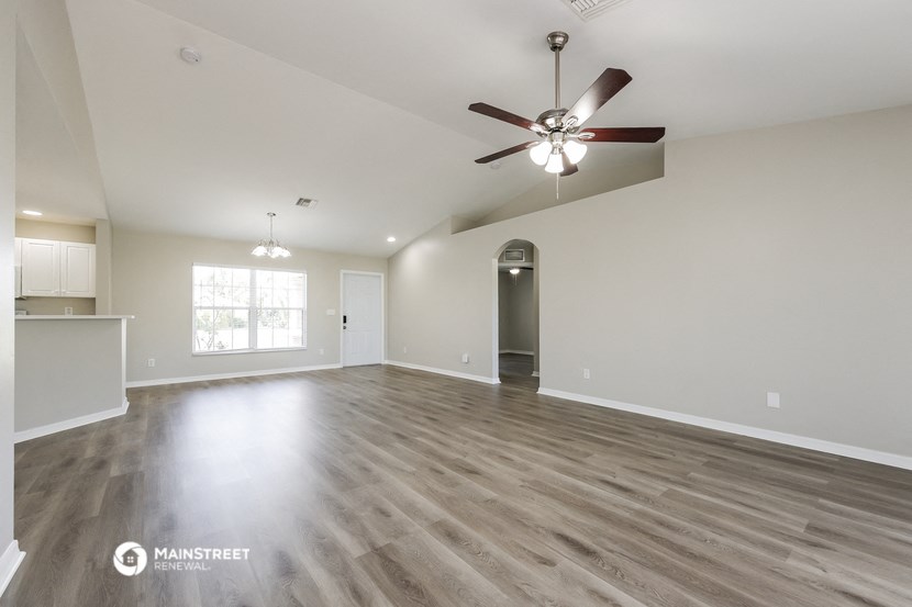 an empty living room with a ceiling fan and a kitchen