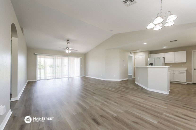 an empty living room with a kitchen and a ceiling fan
