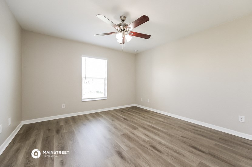 the spacious living room with wood flooring and a ceiling fan