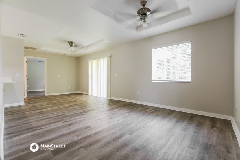 the spacious living room with wood flooring and a ceiling fan