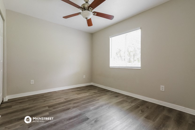 the spacious living room with wood flooring and a ceiling fan