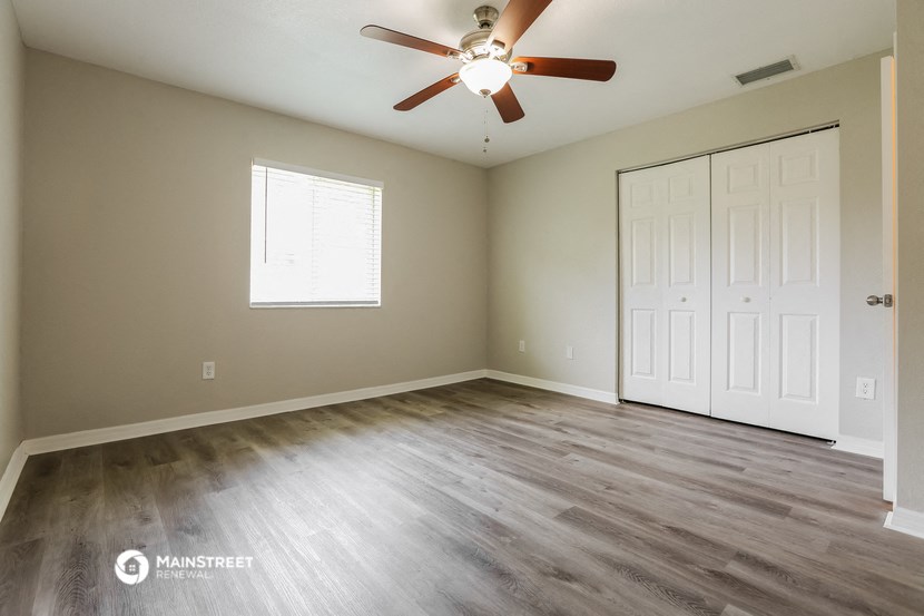 the spacious living room with wood flooring and a ceiling fan