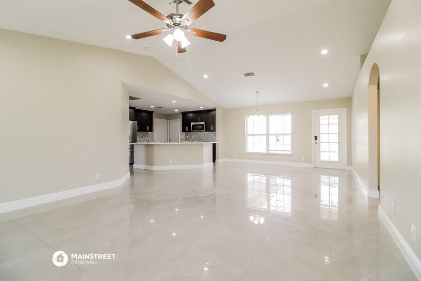 an empty living room with a ceiling fan and a kitchen