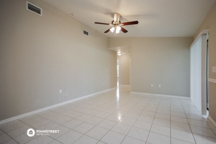 an empty living room with a ceiling fan and a tiled floor