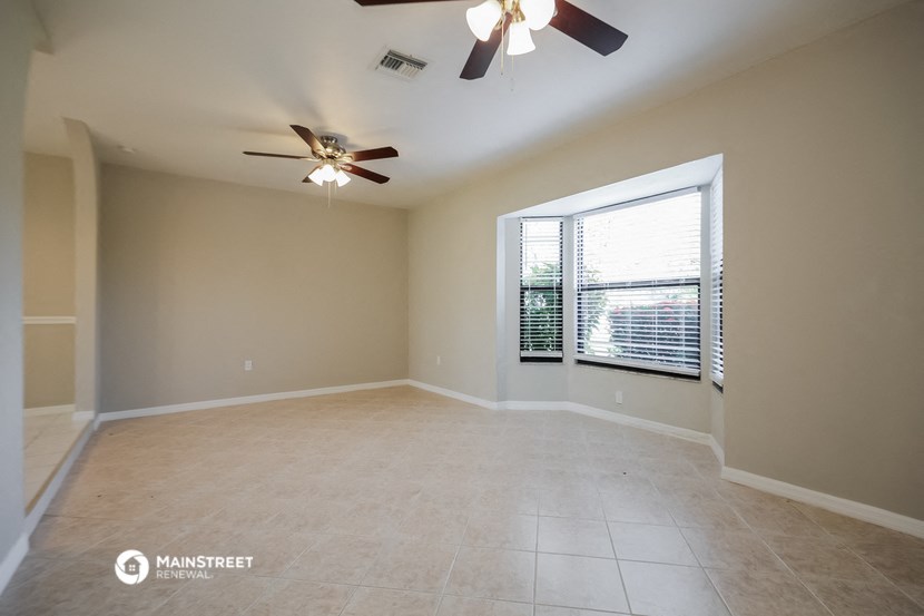 an empty living room with a large window and a ceiling fan