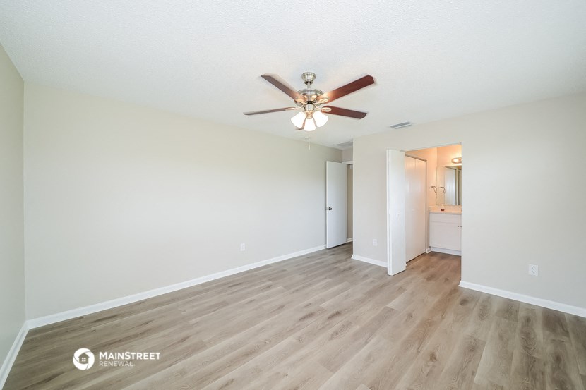 the spacious living room with hardwood flooring and a ceiling fan