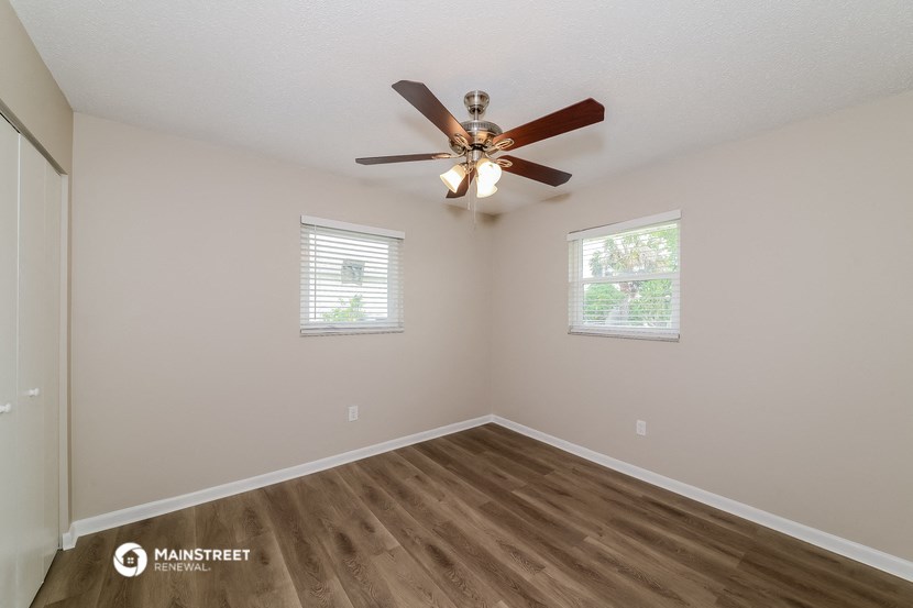 the spacious living room with ceiling fan and two windows